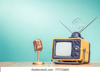 Retro old yellow TV receiver with antenna and golden microphone on wooden table front gradient aquamarine wall background. Vintage instagram style filtered photo