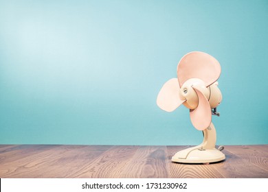 Retro Outdated Portable Office Or Home Electrical Cooling Fan Standing On Table Front Mint Blue Wall Background. Nostalgic Accessory Concept. Vintage Style Filtered Photo