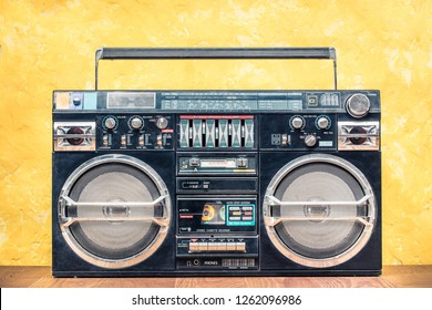 Retro outdated portable stereo boombox radio receiver with cassette recorder from circa 80s front concrete textured yellow wall background. Listening music concept. Vintage old style filtered photo 