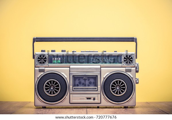 Retro outdated portable stereo boombox radio\
cassette recorder from 80s front yellow background. Vintage\
instagram old style filtered\
photo