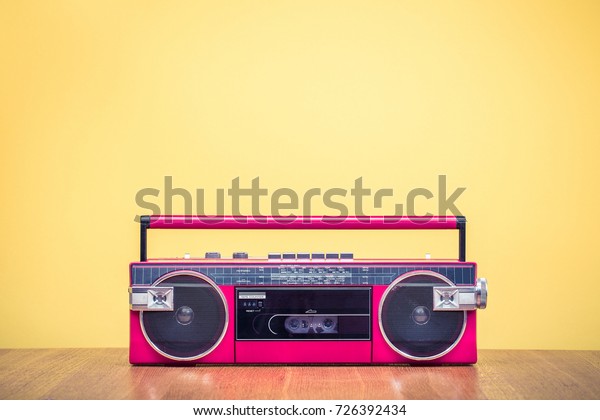Retro outdated red portable stereo radio cassette\
recorder from 80s front yellow background. Vintage old instagram\
style filtered photo