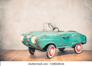 Retro Outdated Rusty Metal Turquoise Pedal Car Toy From Circa Late 60s Or Early 70s In Front Concrete Textured Wall Background. Vintage Style Filtered Photo