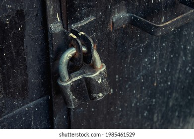 retro padlock on an old iron black door to the basement of a building. The entrance is closed behind an iron door. black iron door with padlock