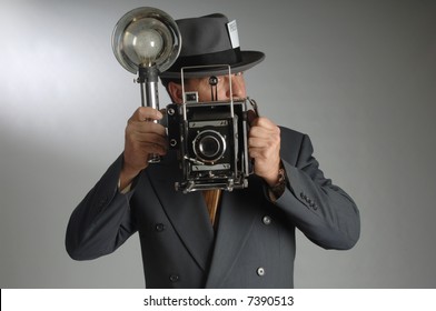 Retro photo journalist wearing a Fedora hat and holding a vintage camera with flash bulb