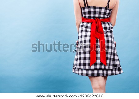 Retro, pin up, elegant and timeless clothes concept. Woman wearing retro checked black and white dress with big red bow, studio shot on blue background