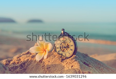 retro pocket watch and plumeria flower on sand sea beach, tropical ocean background. summer vacation, relax time, travel concept. close up