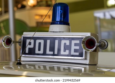 Retro Police Car Sign And Vintage Siren 1980s UK. Selective Focus Close-up Of The Top Of A Police Patrol Car With Flashing Blue Light From The Late 1980s Or Early 1990s. 