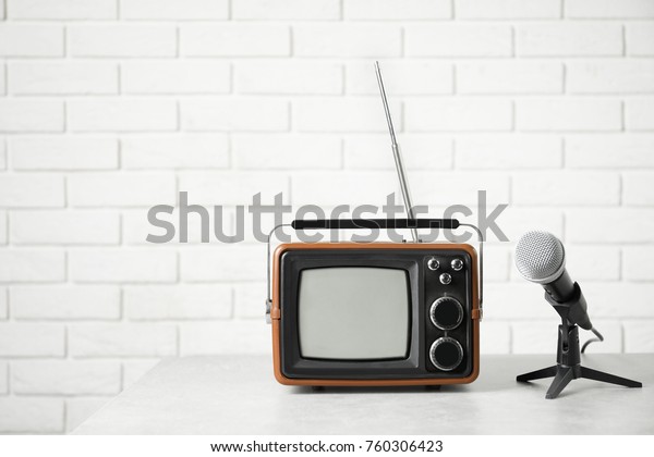 Retro portable TV and microphone on table against\
brick wall