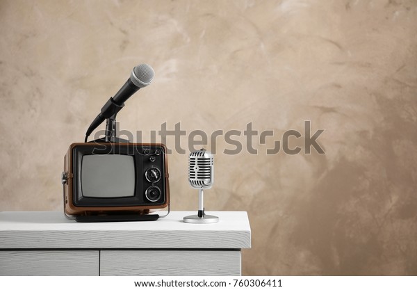 Retro portable TV and microphones on table against\
light wall