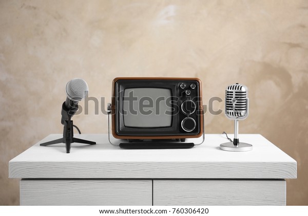 Retro portable TV and microphones on table against
light wall