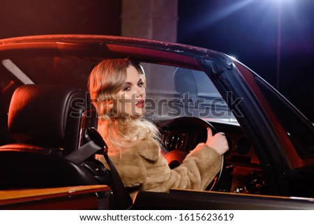 Retro portrait of a beautiful luxury Gatsby woman in black cabriolet car. Vogue fashion style and smoke. Cheerful woman rides to a party. Copy space