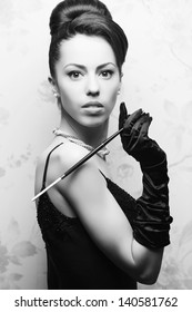 Retro Portrait Of A Beautiful Woman In Great Cocktail Dress Smoking A Cigarette With Holder. Jewelry And Beauty. Vintage (Hollywood) Style. Classic Old Movie Star. Black And White Studio Shot