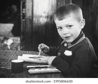 Retro Portrait Of Soviet Boy Drawing With Paints On Paper. Vintage Black And White Paper Photo. Early 1960s. Old Surface, Soft Focus. Transferred Property, Family Archive.