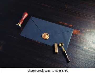 Retro postal stationery. Black envelope with golden wax seal, stamp and spoon on dark wooden background.