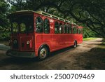 retro red tour bus or trolley parked under beautiful live oaks in Charleston South Carolina