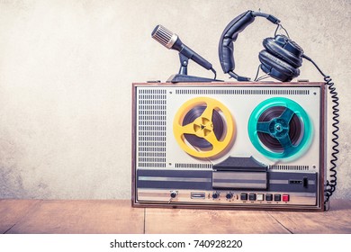 Retro Reel To Reel Tape Recorder, Microphone And Headphones On Wooden Table Front Concrete Wall Background. Vintage Style Filtered Photo