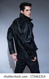 Retro Rock And Roll 50s Fashion Man With Dark Grease Hair. Wearing Black Leather Jacket And Jeans. Studio Shot Against Grey.