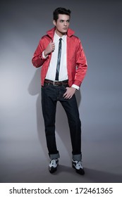 Retro Rock And Roll Fifties Fashion Man With Dark Grease Hair. Wearing Red Jacket And Jeans. Studio Shot Against Grey.