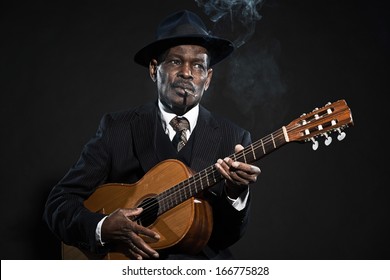 Retro Senior Afro American Blues Man. Wearing Striped Suit With Blue Hat. Playing Acoustic Guitar. Smoking Cigar.