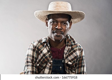 Retro Senior Afro American Blues Man In Times Of Slavery. Wearing Denim Bib And Brace Overall With Straw Hat.