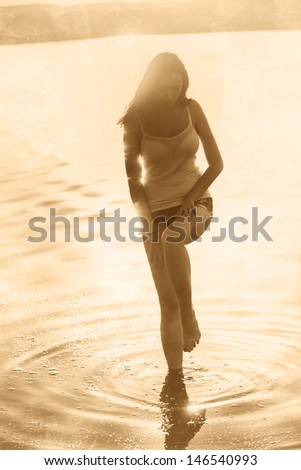 retro sepia silhouette of a young beautiful woman girl at sunset on the beach in the water sea ocean