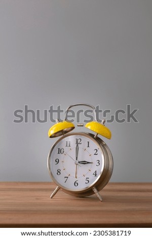 Retro silver alarm clock. 3:00.  am,  pm. Neutral background. Brown wood surface. Vertical photography with empty space for text or image.