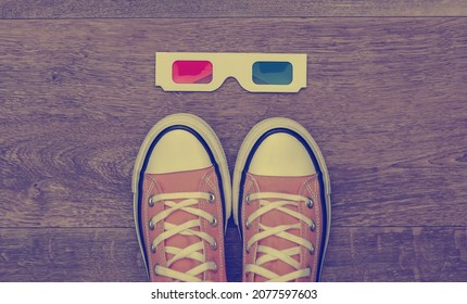 Retro sneakers (gumshoes) with 3d glasses on wooden floor. Top view. Flat lay