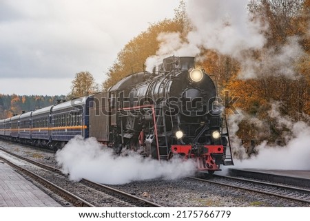 Retro steam train departs from the station wooden platform at cloudy autumn evening.