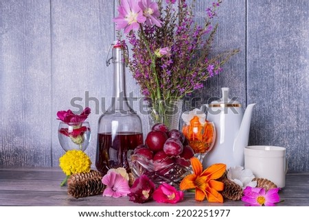 Retro still life with bouquet of summer wild flowers, decanter of red wine, wine glasses and vase with ripe plums on wooden table.