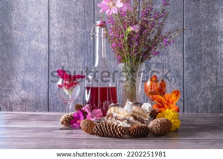 Retro still life with bouquet of summer wild flowers, decanter of red wine, wine glasses and fir cones on wooden table.
