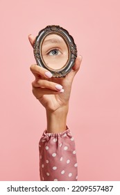 Retro style. Female hand holding small mirror with reflection of girl's eye isolated over pink background. Concept of vintage fashion, beauty, art, creativity and ad. Human emotions, facial expression