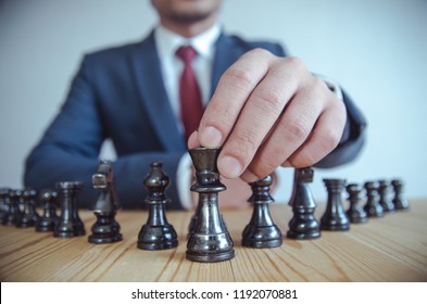 Retro style image of a businessman with clasped hands planning strategy with chess figures on an old wooden table. - Shutterstock ID 1192070881