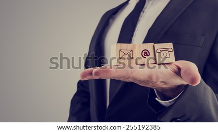 Retro style image of a businessman holding three wooden cubes with contact symbols - envelope, at sign and telephone - conceptual of communication and business support.