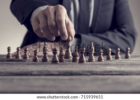 Retro style image of a businessman playing a game of chess on an old wooden table in a close up view of his hand moving a piece conceptual of strategy, planning and skill.