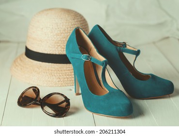 Retro style image of female fashion: straw hat, sun glasses and turquoise shoes over white wooden background. Selective focus, shallow DoF, vintage filters