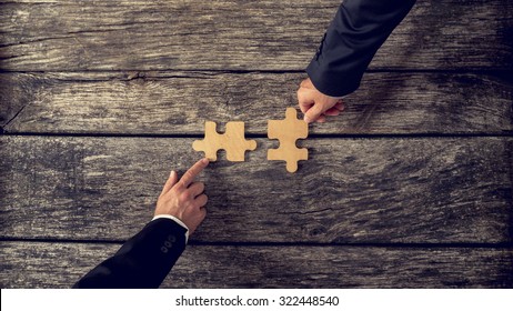 Retro style image of two business partners each placing one matching piece of puzzle on a textured wooden table. Conceptual of cooperation, innovation and success.