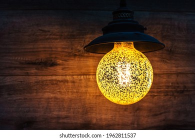 Retro Style Lamp On A Background Of A Wooden Wall. Round Chandelier With Bright Yellow Light And Black Metal Shade. Copy Space