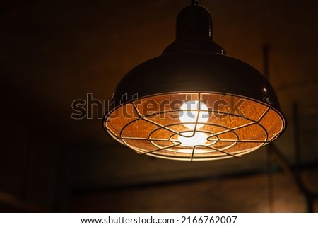 A retro style metal ceiling lighting lamp with warming light glowing bulb. Interior decor, selective focus object. Photo contained some noise and high constrast ratio due to low light condition.