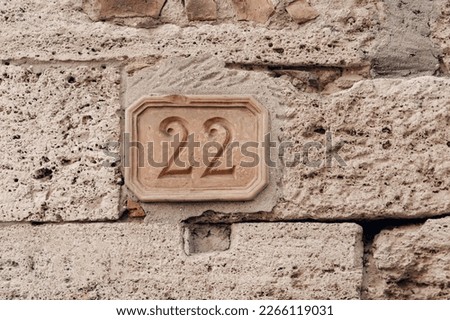 Retro style pastel nameplate with carved in stone figures of two and two. 22 plaque. House number twenty-two on old brick ancient wall. Architectural details. Italy.