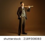 Retro style portrait of young man in image of english gangster, businessman wearing suit and cap standing isolated over dark vintage background. Concept of business, personality, emotions, fashion