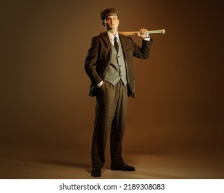 Retro style portrait of young man in image of english gangster, businessman wearing suit and cap standing isolated over dark vintage background. Concept of business, personality, emotions, fashion