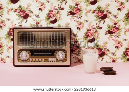 Retro style radio, a glass of milk and chocolate cookies, creative 50s nostalgia inspired layout against old fashioned floral wallpaper.
