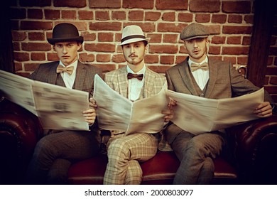 Retro Style. Three Handsome Men In Elegant Suits Sit On A Leather Sofa And Read Newspapers. Newspaper Editorial Office. Men's Fashion. Men's Club. 