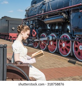 retro style. Woman traveler sitting on wooden bench on platform of Railway Station. Near old train . Cute lady wait train and read the vintage book Girl wear long white dress Leather case stand near  - Powered by Shutterstock