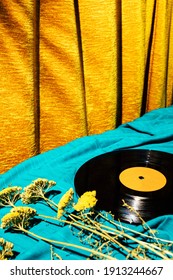 Retro styled image of LP vinyl record on a cyan silk or saten fabric with dry old flowers and gold orange curtain in the background. Analog hipster creative concept. - Shutterstock ID 1913244667