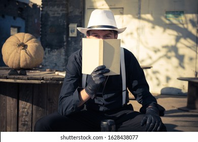 Retro styled man looking at camera while hiding his face behind a book. 