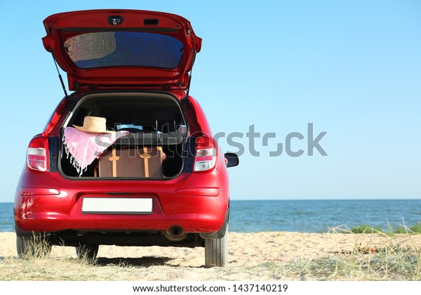 Retro suitcase and beach accessories in car\
trunk on sand near sea. Space for\
text
