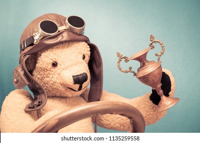 Retro Teddy Bear Toy In Leather Pilot's Hat And Vintage Goggles With Award Winner's Cup Front Mint Green Wall Background. Old Style Filtered Photo