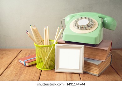 Retro telephone, pencils, frame and old books on wooden table