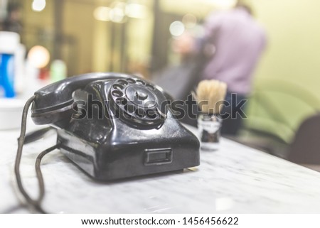 Retro telephone and shaving brush on table at barber shop. Hair salon appointment scheduling concept.